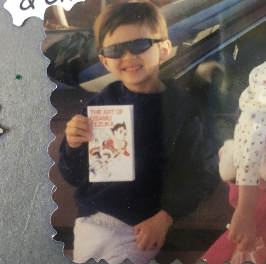 Tiny toddler Dylan wearing cool epic shades and holding a book titled The Art of Osamu Tezuka.