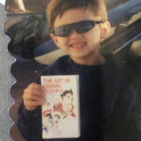 Tiny toddler Dylan wearing cool epic shades and holding a book titled The Art of Osamu Tezuka.
